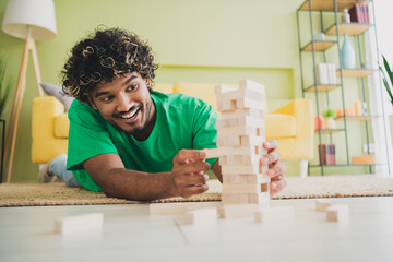 Portrait of nice young man playing jenga blocks wear t-shirt modern green interior flat indoors
