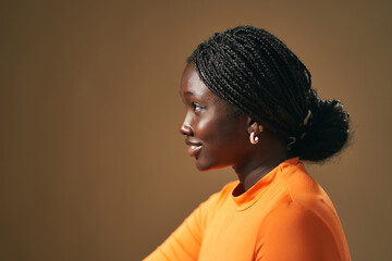 Young black woman with braids smiling in profile on brown background