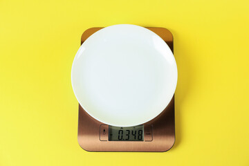 Electronic kitchen scale with empty plate on yellow background, top view