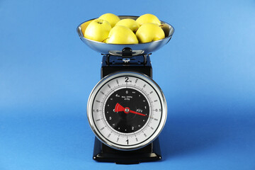 Mechanical kitchen scale with bowl of apples on blue background