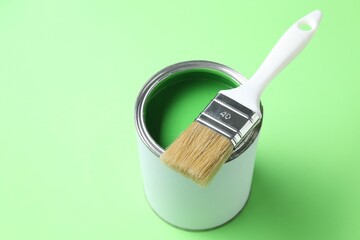 Can of bright paint and brush on light green background, closeup