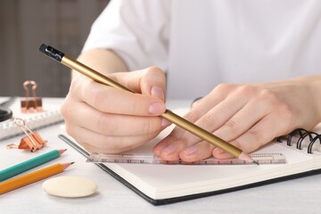 Woman drawing sketch with ruler and pencil on notebook at light table, closeup