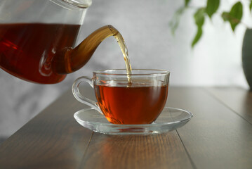 Pouring freshly brewed tea from teapot into cup at wooden table, closeup