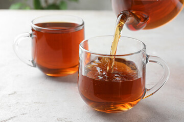 Pouring aromatic tea from teapot into cup at light textured table, closeup