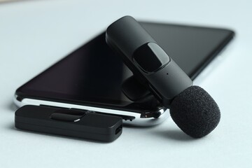 Lavalier microphone and smartphone with wireless receiver on light background, closeup