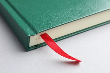 Book with red ribbon bookmark on light grey table, closeup
