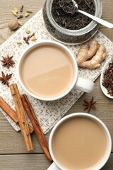 Aromatic Masala tea in cups, dry leaves and spices on wooden table, flat lay