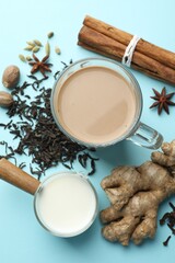 Aromatic Masala tea in glass cup, spices, dry leaves and milk on light blue background, flat lay