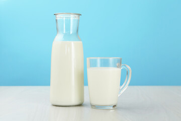 Fresh milk in cup and jug on white wooden table against light blue background