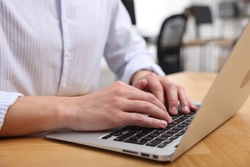 Man working on laptop at wooden desk in office, closeup