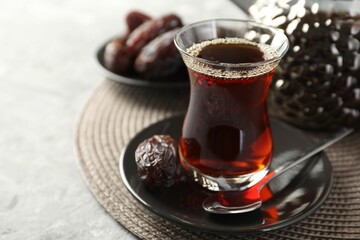 Traditional Turkish tea in glass cup and dates on light grey table, closeup. Space for text