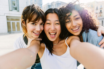 Three multiracial young women having fun on city street. Millennial group of female friends...