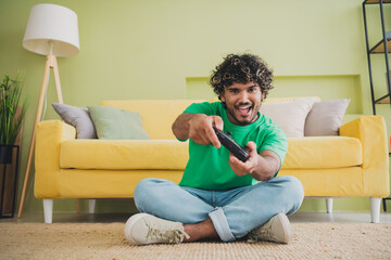 Full length portrait of nice young man sit floor play video games wear t-shirt modern green...