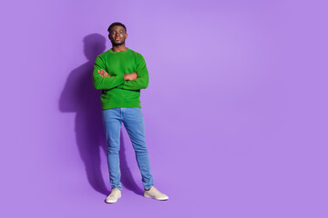 Fototapeta premium Portrait of a casually dressed young man wearing a green pullover standing confidently before a purple backdrop