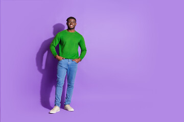 Young man in casual green sweatshirt and jeans smiling confidently against a purple background, expressing modern style and happiness