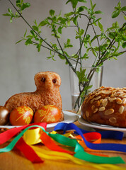 Easter still life containing a small lamb cake, painted eggs, traditional Czech Easter sweet cake called "mazanec", an Easter whip and green twigs in a vase. Czech and Slovak Easter still life