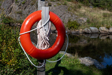 An orange plastic lifebuoy or life ring hanging on a wooden post with a long white braided rope...