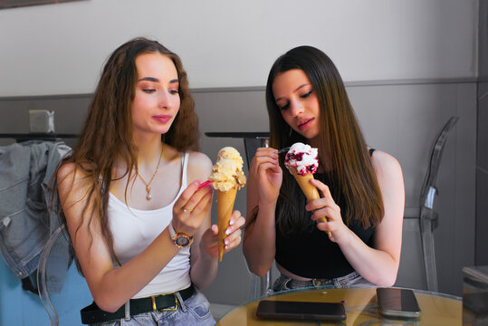 Young friends savoring ice cream cones indoors at a cafe table