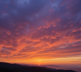 Fototapeta premium A breathtaking sunset view showcasing majestic mountains silhouetted against a vibrant sky, with hues of orange, pink, and purple blending seamlessly into fluffy clouds.