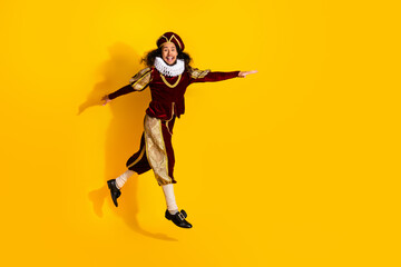 Young man in medieval noble costume jumping joyfully on bright yellow background showcasing fun and...