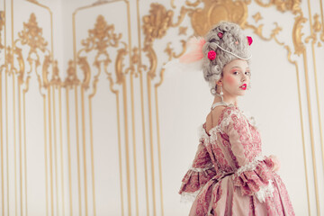 A young woman in vintage baroque attire poses gracefully against an ornate interior.