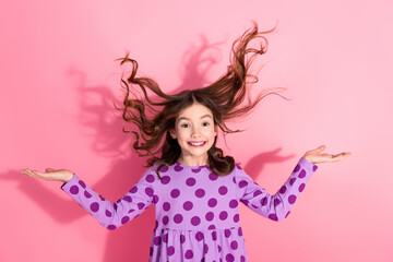 Adorable young girl with wavy brown hair in a polka-dot dress posing against a vibrant pink...