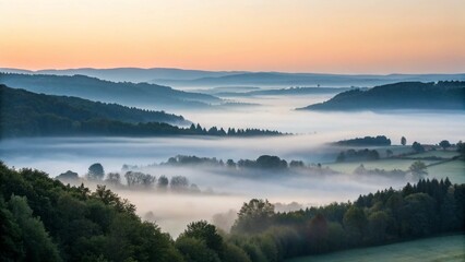 Fototapeta premium This image captures a tranquil scene of fog-filled valleys between tree-covered hills, illuminated by the gentle colors of sunrise or sunset