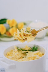 A ceramic bowl containing pasta topped with grated cheese and garnished with dill. Stylish utensils and yellow roses in the background create a cozy and appealing presentation.