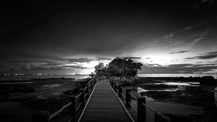 Black and white photo of a bridge over the sea at sunset.