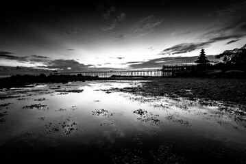 Black and white photo of a bridge over the sea at sunset.