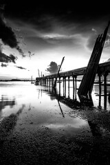 Black and white photo of a bridge over the sea at sunset.