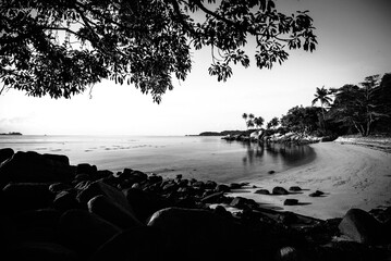 Black and white photo of a bridge over the sea at sunset.
