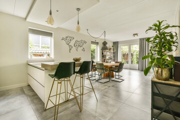 A stylish kitchen and dining space featuring a world map on the wall, modern furniture, and natural light streaming through windows, creating a warm atmosphere.