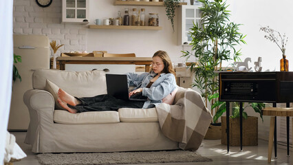A woman in a denim jacket sits on a couch, focused and thoughtful, holding a notebook and pen while...