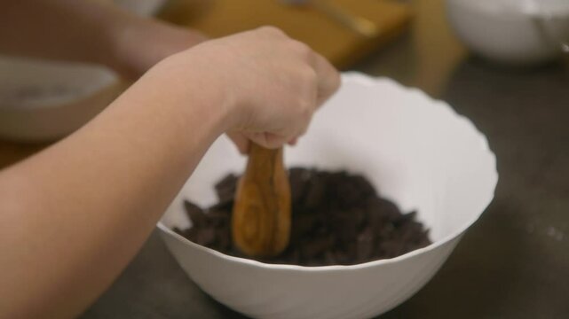 Hand and arm of a teenage girl in a domestic kitchen, crushing black biscuits in a white bowl.  Night. Close-up, spotlight in hand