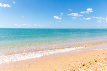 Sunny beach with a turquoise ocean in the background. Sea waves near the tropical coast on a sunny day. Cruise. Landscape of a summer sea beach with white sand and shells. Travel concept.