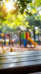 Sunlight filters through blurred green leaves, casting a warm glow on an empty wooden bench with a colorful playground softly out of focus in the background.