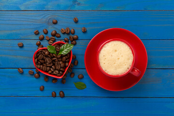 Cup of coffee with coffee beans and leaves on wooden background,top view