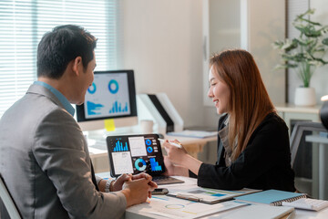 Asian businesspeople discussing statistics graphs on tablet and desktop computer in office meeting room