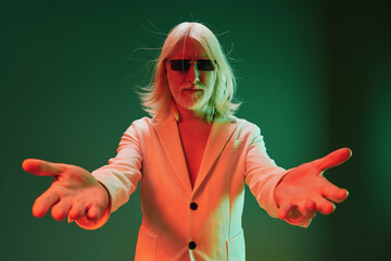 Stylish man in a white blazer extending arms, standing against a green background with dramatic...