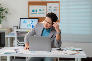 Stressed Asian businessman having problems and touching his head at office desk