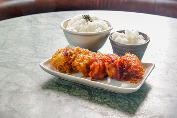 Crispy and Spicy Korean fried chickenon white plate with pickled radish,rice on marble table,Traditional Korean food,Korean foods served on a dining table,The street food of Korea.