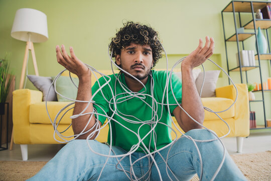Photo of nice young man shrug shoulders hold tied cable wear t-shirt modern green interior apartment indoors