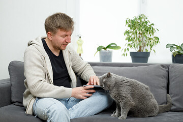 Man on the couch in the living room playing with the cat