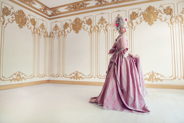 Fototapeta premium Elegant woman in a flowing pink gown standing in a lavishly decorated room with ornate gold details