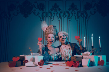Elegant couple in baroque costume holding hearts indoors in a vintage themed setting