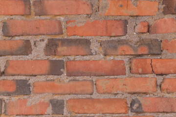 Grunge background of orange wall made of bricks bonded with cement of abandoned old building.