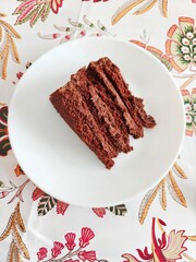 Chocolate cake on a white plate and a colorful tablecloth.