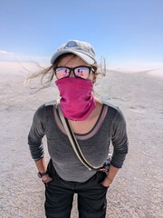 Caucasian woman tourist in scarf and goggles standing in desert wilderness; survival, fashion,...