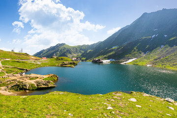 balea lake of romania. alpine landscape of fagaras mountains with pond. sunny weather with clouds on the blue sky above carpathians. snow and grass on the hillside in summer. idyllic place